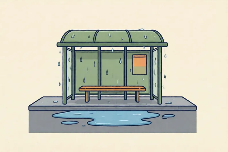 A wet bus stop on a grey street with a puddle and no people