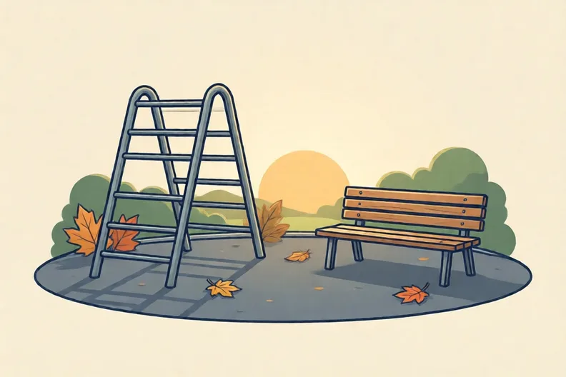 An empty school playground with a climbing frame, a wooden bench and autumn leaves.