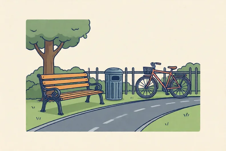 A park bench beside a path with a litter bin and a bicycle leaning on a fence