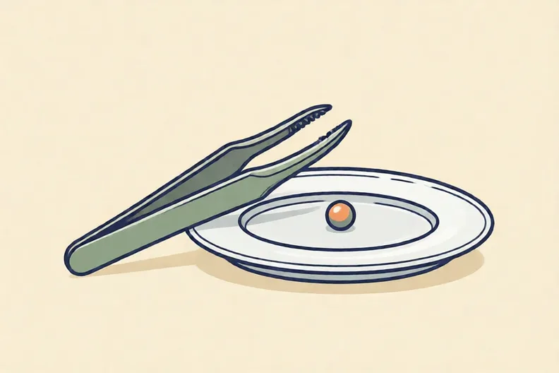 A pair of metal tweezers lying beside a small bead on a plate