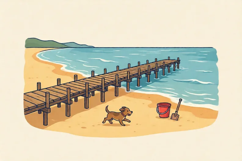 A sandy beach with a pier, a dog, a bucket and a spade