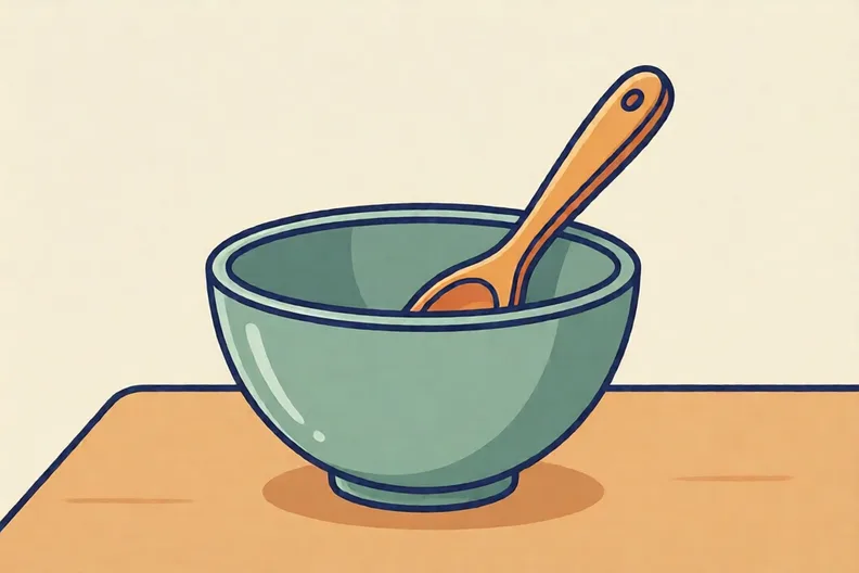An empty mixing bowl with a wooden spoon on a kitchen table