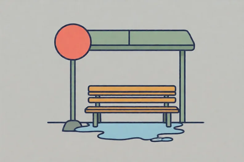 An empty bus stop on a grey background with a red sign, a bench and a puddle.