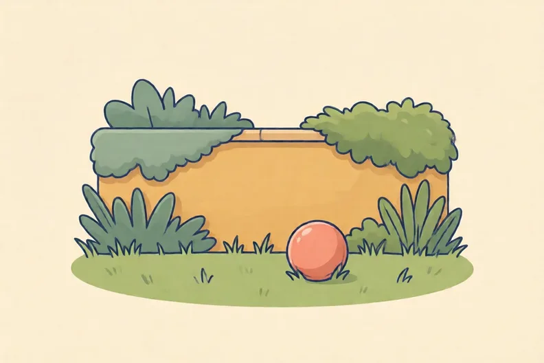 A garden wall with a soft ball resting on short grass in front of it, no people