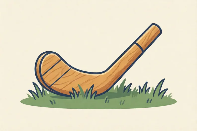 A wooden hockey stick lying on grass, with its flat side and curved back both visible