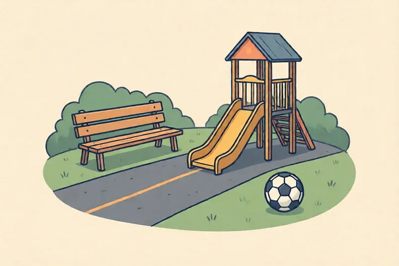 An empty playground at lunchtime with a bench and a football on the grass