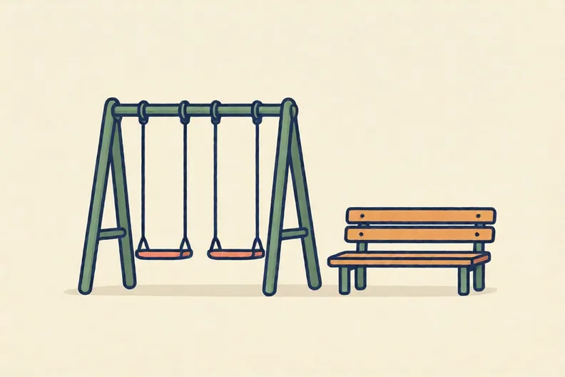 An empty school playground with a swing set and a wooden bench