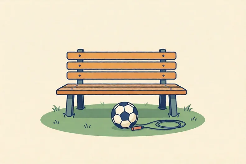 A park bench in the sun with a football and a skipping rope on the grass