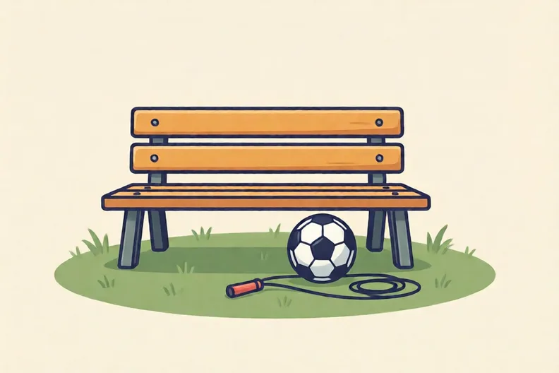A park bench in the sun with a football and a skipping rope on the grass