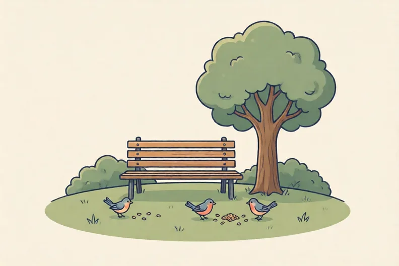 A park bench beside a tree, with bird seed on the grass and small birds feeding