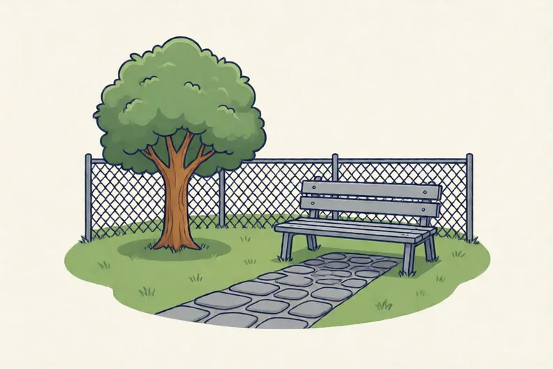 Grass, a small tree, a bench and a stone path by a playground fence.